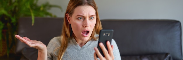 Malheureuse femme assise sur un canapé avec un ordinateur portable et parler au téléphone à la maison.