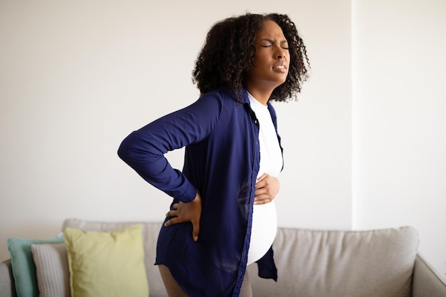 Photo malheureuse femme enceinte afro-américaine millénaire désespérée avec un gros ventre souffrant de maux de dos