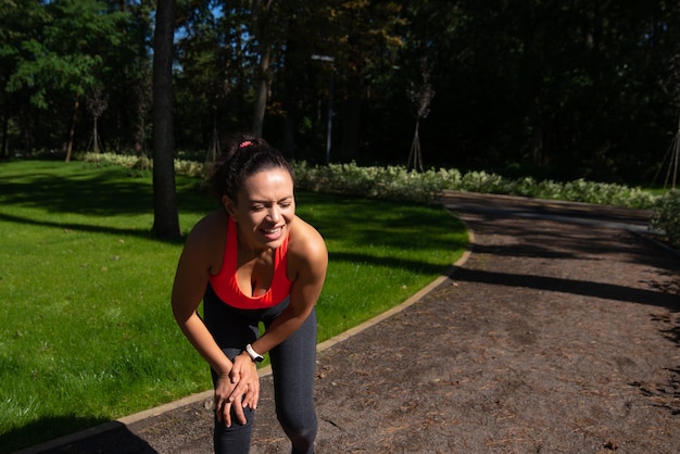 Une malheureuse femme en forme ressentant une douleur au genou pendant le sport et l'entraînement en plein air