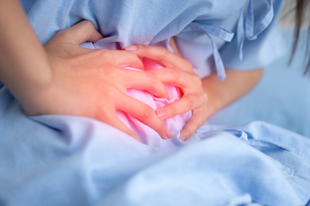 Malheureuse femme patiente asiatique assise sur le lit d'hôpital et tenant sur l'estomac souffrant