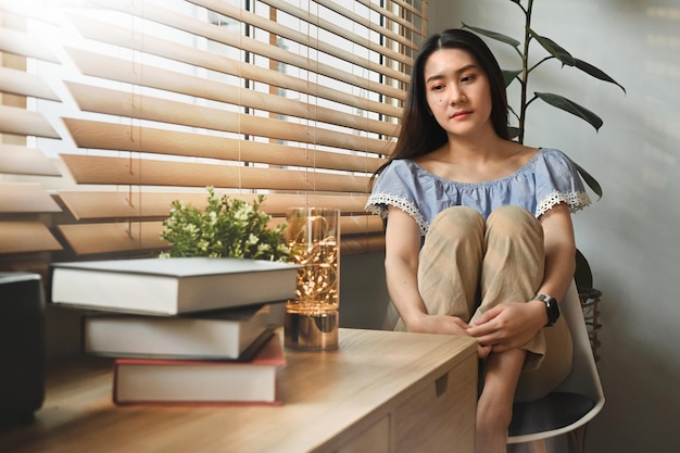 Malheureuse jeune femme assise sur une chaise embrassant les genoux se sentant désespérée un concept de soins de santé mentale solitaire