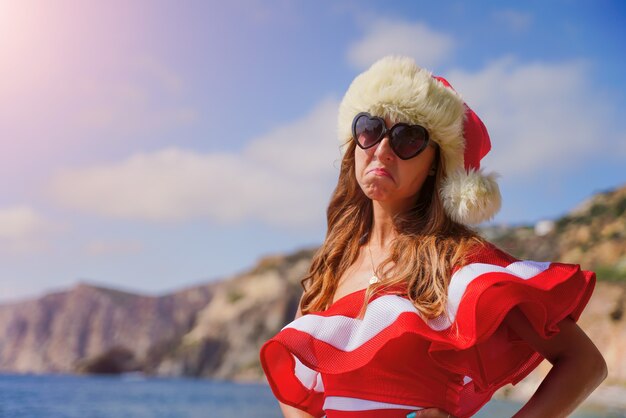 Malheureuse jeune femme brune séduisante en maillot de bain rouge et bonnet de noel sur la plage vacances de Noël