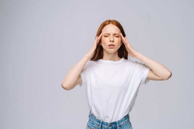 Malheureuse jeune femme en t-shirt et pantalon en jean massant les temples ressentant une douleur terrible migraine