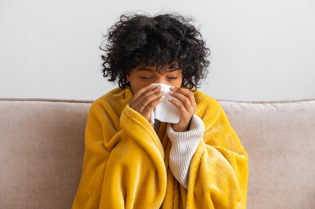 Malheureuse malade jeune femme afro-américaine avec froid assis sur un canapé à la maison fille couvrant de blanc