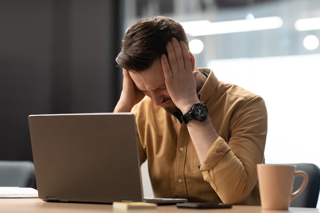 Malheureux homme d'affaires près d'un ordinateur portable touchant la tête ayant des maux de tête au bureau