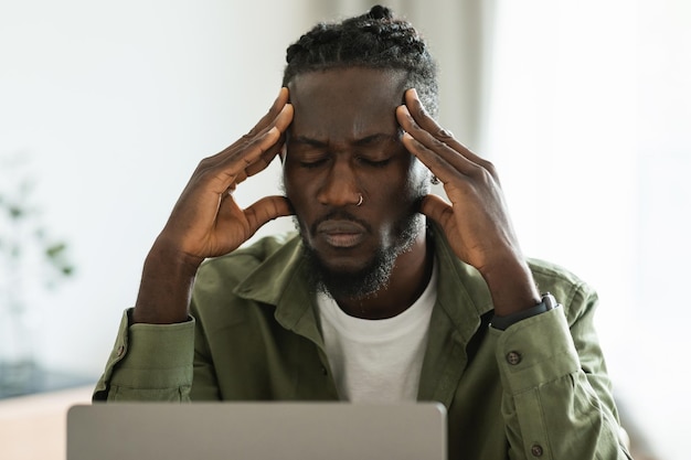 Malheureux pigiste noir touchant la tête souffrant de maux de tête ou ayant des problèmes de travail assis au bureau