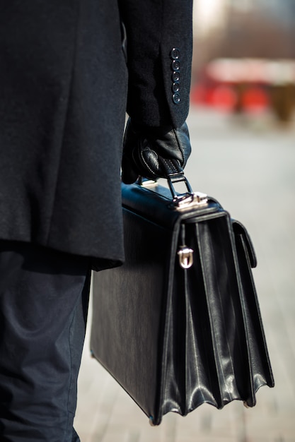 mallette en cuir à la main. jeune homme d'affaires marchant dans la rue.