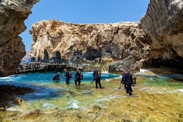 Malte La Valette 16 juin 2019: De nombreux plongeurs dans l'équipement entrent dans l'eau bleue et pure d'un petit canyon par une journée ensoleillée. Le canyon est entouré de grosses pierres.