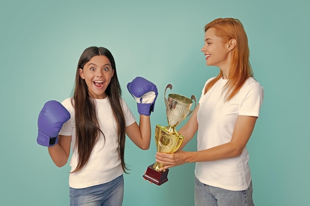 Maman et adolescent enfant fille tenant le prix gagnant montrant le trophée sur fond bleu Soutien parental fille enfant célébrant la victoire Adolescent boxeur gagnant boxe