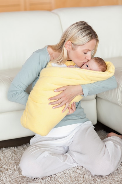 Maman affectueuse embrassant son bébé qui est enveloppé dans une couverture