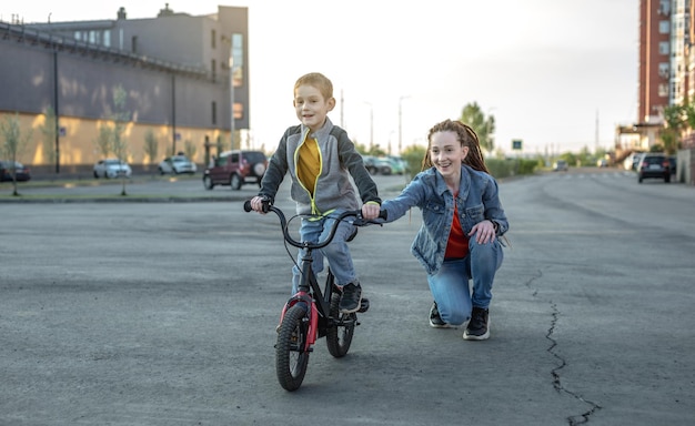 Maman aide un enfant garçon à apprendre à faire du vélo à deux roues dans le parc Agréables vacances sportives d'été pour enfants