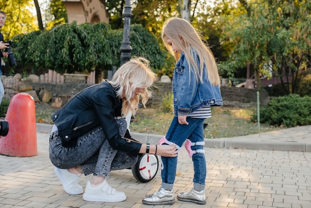 Maman aide à habiller l'équipement et le casque de sa petite fille pour une balade en Segway dans le parc