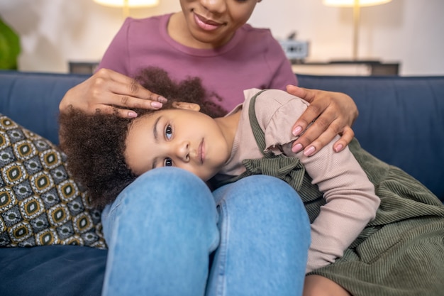 Maman amour. Femme afro-américaine souriante tendre attentionnée touchant la tête de mentir triste jolie fille à la maison dans l'après-midi