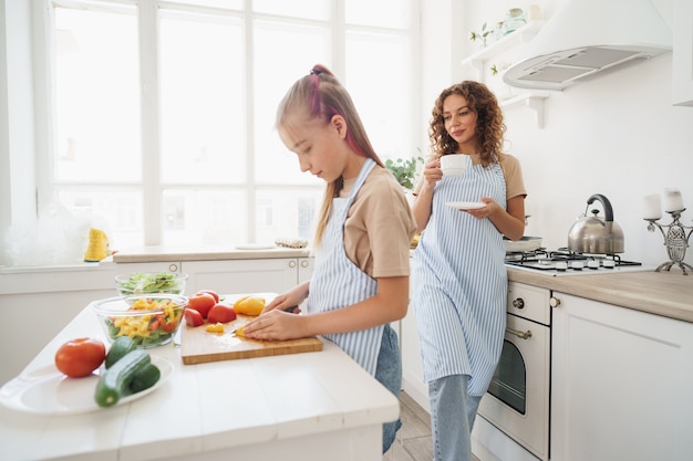 Maman apprend à sa fille adolescente à cuisiner une salade de légumes dans la cuisine