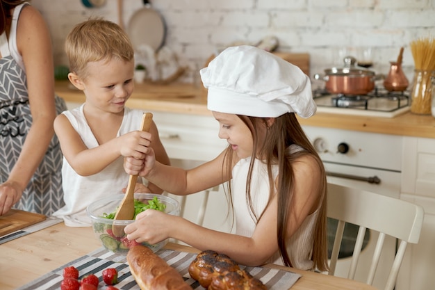 Maman apprend à sa fille et son fils à préparer une salade de légumes frais