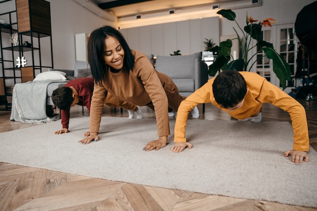 Maman apprend à ses deux fils à faire des exercices physiques sportifs le matin à la maison. Photo de haute qualité