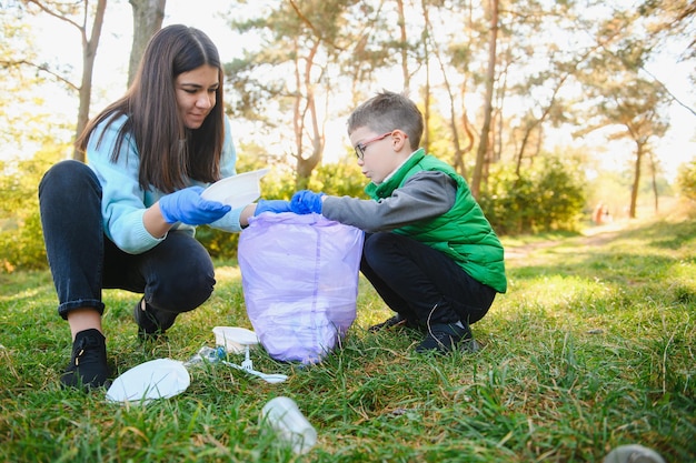 Maman apprend à son fils à nettoyer les déchets dans la nature. Une femme retire des bouteilles en plastique dans un sac. Le sujet de la pollution de l'environnement par les ordures.