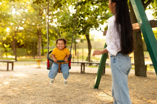 Maman asiatique balançant sa petite fille sur une balançoire à l'extérieur dans le parc
