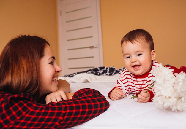 Maman aux longs cheveux roux joue avec le petit garçon sur le lit