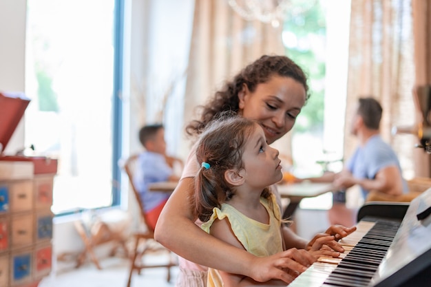 Maman ou baby-sitter apprend à une petite fille à jouer du piano, observe attentivement les mouvements des doigts de l'enfant et sourit.