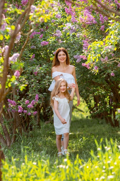 Maman avec un bébé dans ses bras lors d'une promenade dans le jardin de lilas de printemps dans le concept de parc de famille heureuse