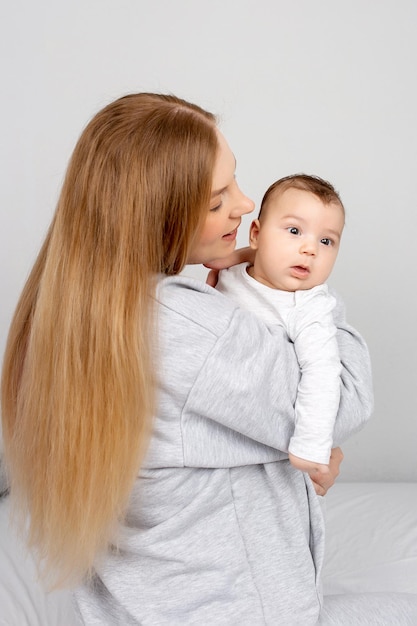 Maman et bébé jouent sur le lit Mère et fils famille heureuse belle fille blonde et bébé mignon à la maison