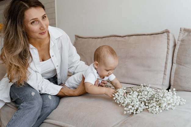 maman et bébé sur le lit avec un bouquet de fleurs blanches