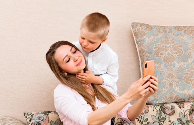 Maman et bébé prenant un selfie dans un salon confortable. maman et son fils font des grimaces et se prennent en photo devant la caméra