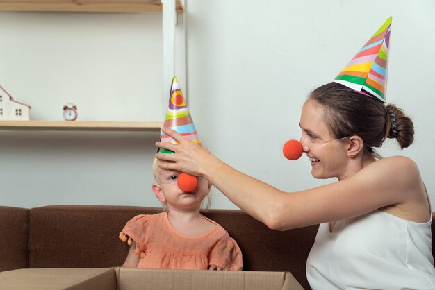 Maman et bébé se préparent pour les vacances. Maman met un chapeau de fête et un nez de clown pour sa petite fille.