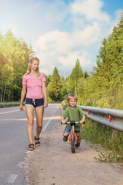 Maman blonde active marchant avec un enfant à vélo Sport familial