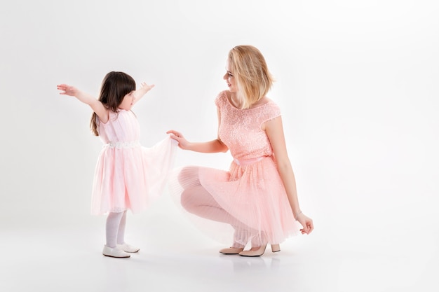 Maman blonde et douce petite fille en robes roses princesses étreignant et riant sur fond gris. famille