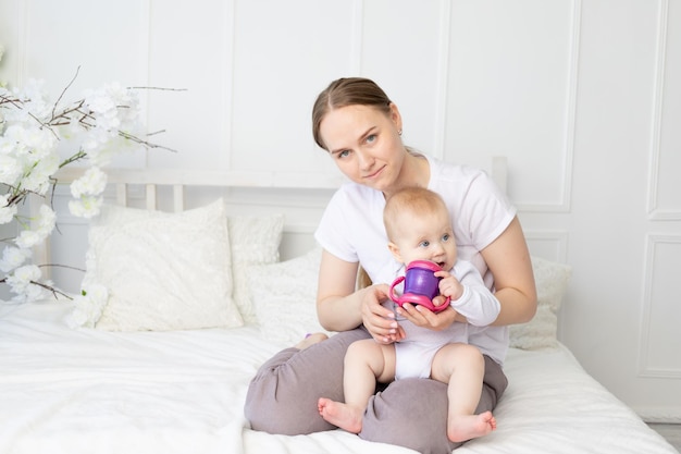 Maman boit ou nourrit au biberon un bébé sur un lit blanc à la maison concept d'aliments pour bébés