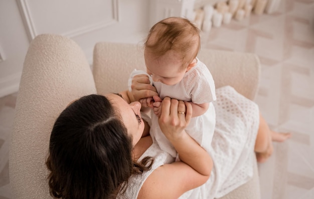 Maman brune caucasienne est assise sur une chaise et joue avec une petite fille