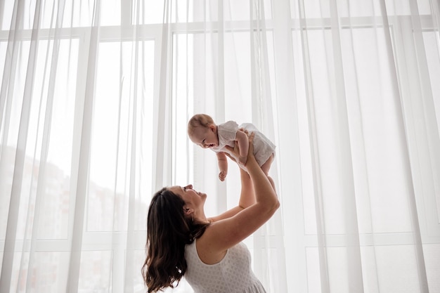 Une maman brune caucasienne avec une petite fille joue devant la fenêtre de la chambre