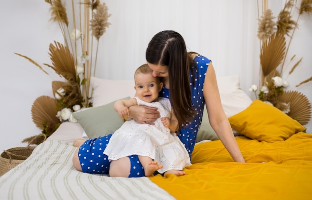 Maman brune embrasse sa fille dans une robe blanche sur le lit dans la chambre