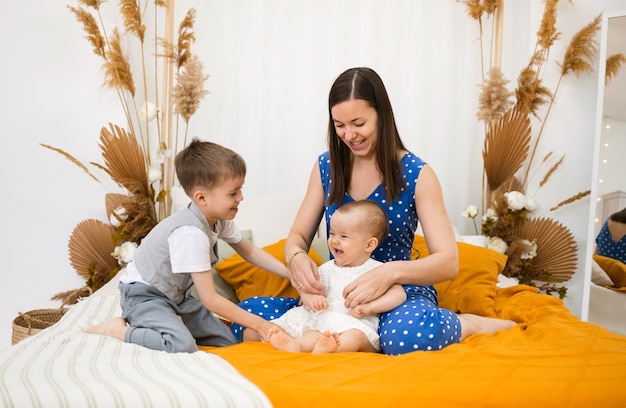 Maman brune est assise sur le lit et joue avec son petit fils et sa fille dans la chambre