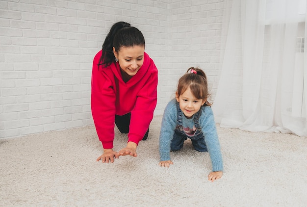 Une maman caucasienne souriante est assise sur le sol du salon et joue avec sa petite fille. Heureuse mère aimante s'amuser avec une petite fille le week-end à la maison familiale.