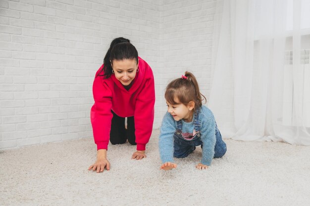 Une maman caucasienne souriante est assise sur le sol du salon et joue avec sa petite fille. Heureuse mère aimante s'amuser avec une petite fille le week-end à la maison familiale.