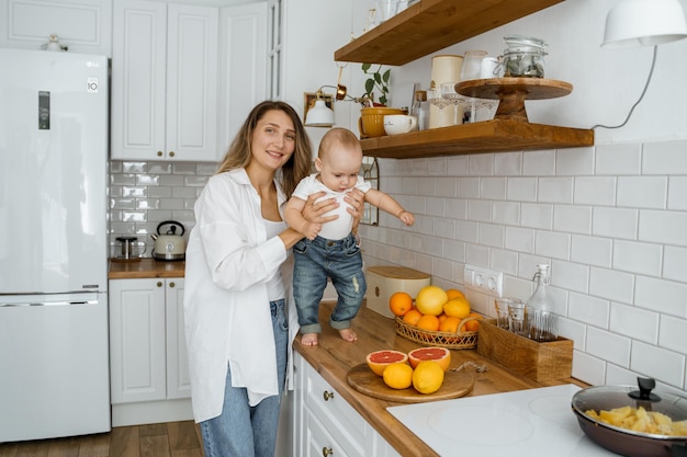 maman en chemise blanche coupe des fruits pour le petit déjeuner à côté de son fils dans une cuisine blanche