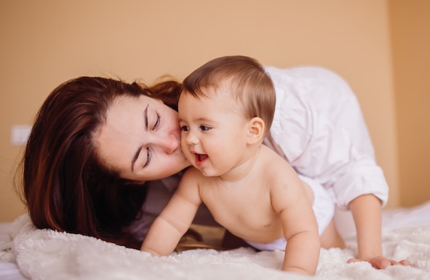 Maman en chemise blanche joue avec le petit garçon sur le lit blanc