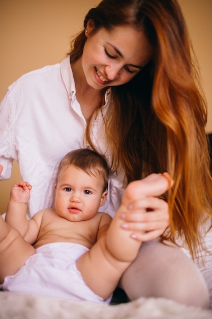 Photo maman en chemise blanche joue avec le petit garçon sur le lit blanc