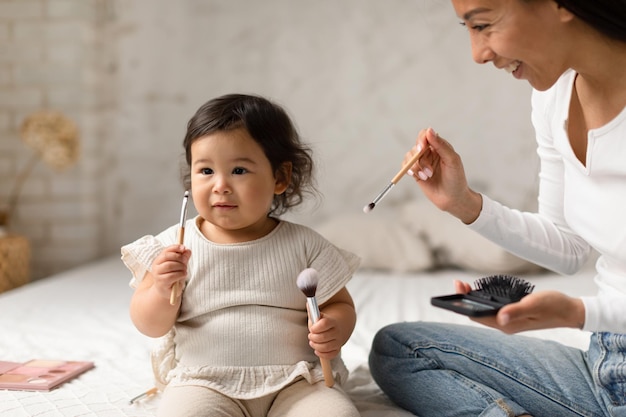 Maman chinoise joyeuse se maquillant et jouant avec sa fille à l'intérieur