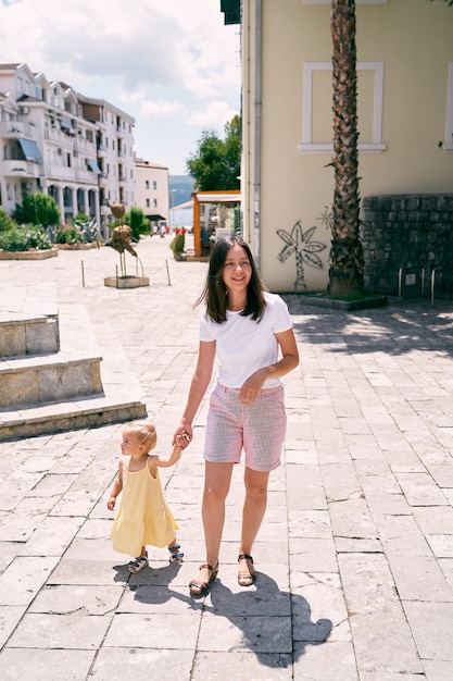 Maman conduit une petite fille le long d'une route pavée avec des maisons en arrière-plan