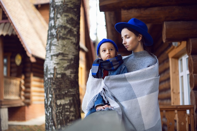 Maman dans un pull et un chapeau bleu avec un enfant assis sur le porche