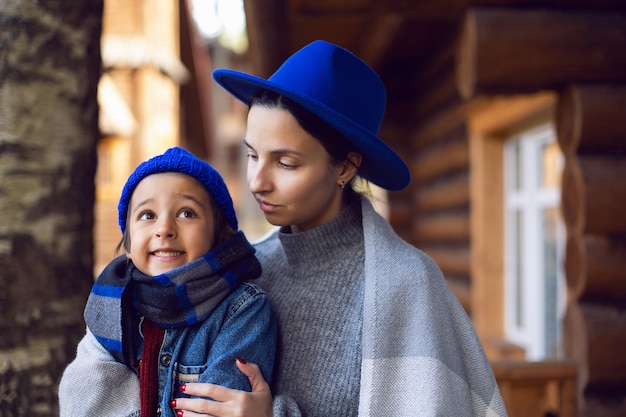 Maman dans un pull et un chapeau bleu avec un enfant assis sur le porche