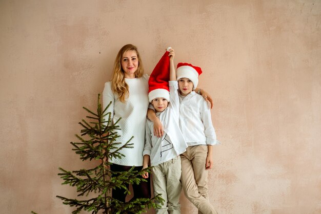 Maman et deux fils par un mur rose et un arbre de Noël. minimalisme.