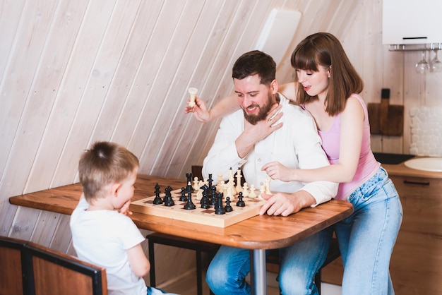 Maman enceinte regardant papa et fils jouer aux échecs à la table