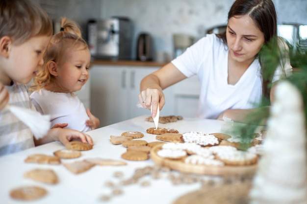 Maman et enfants décorent le pain d'épice de Noël à la maison un garçon et une fille peignent avec des cornets avec sug...