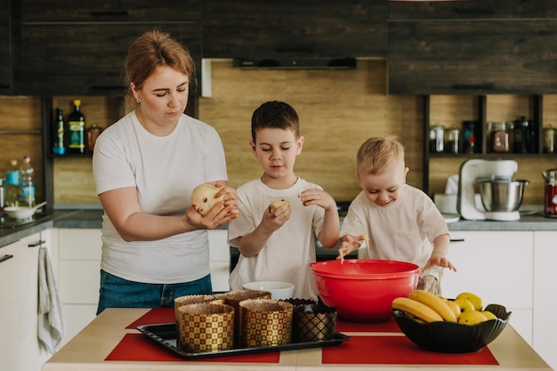 maman avec enfants pétrit la pâte pour de délicieuses pâtisseries qu'ils préparent dans la cuisine à la maison