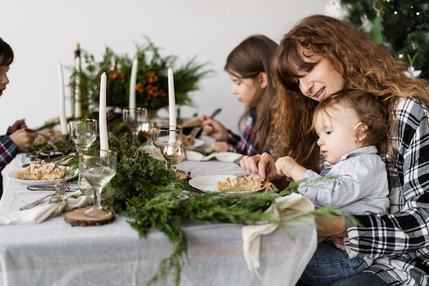 Maman et les enfants prennent le petit déjeuner le jour de Noël à une table décorée de fête dans le salon lumineux le matin La famille mange à table